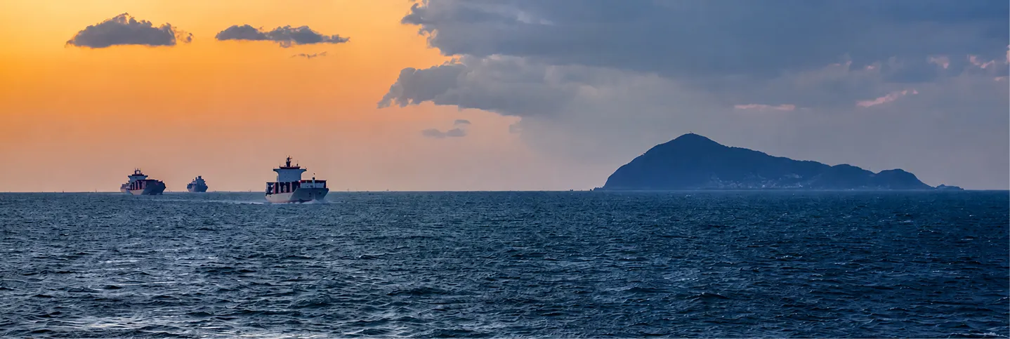 オレンジ色に染まる夕空のもと、落ち着いた青い海をゆく船と、水平線上に浮かぶ島々のシルエット。