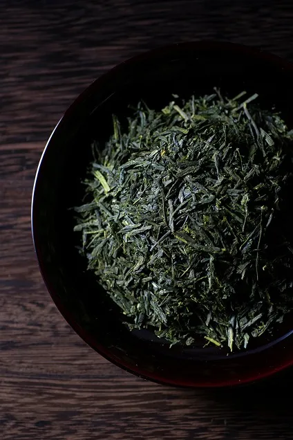 漆器のような黒い丸皿の上に盛られた、ツヤのある色鮮やかな煎茶の茶葉。